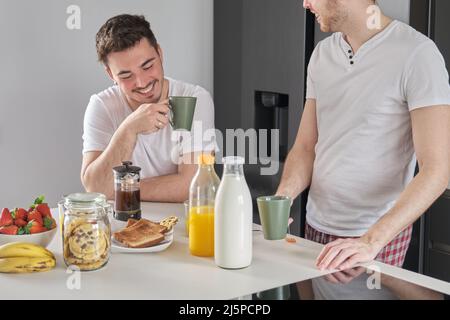 Young gay couple having breakfast, talking and laughing. Stock Photo