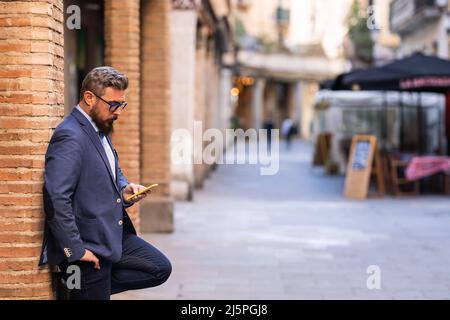 Businessman using a mobile phone while leaning on a column outdoors in the street. Stock Photo