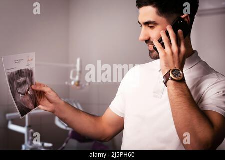 Dentist looking an X-ray of jaw with an implanted tooth. talking on the phone Stock Photo