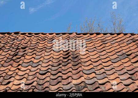 An old red tile roof against a blue sky. Background image Stock Photo