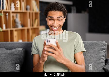 Handsome man sending messages on the smartphone, sitting on the comfortable couch with a cell phone in hands, texting, scrolling and web surfing Stock Photo