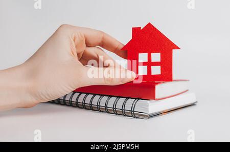 Sweet home. Estimating and paying house tax. Woman holding red house with her hands and notepad in copy space white background, insurance Stock Photo