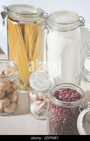 spaghetti pasta, wheat flour, beans and nuts in glass jars, kitchen supply, eco storage. vertical shop. Stock Photo