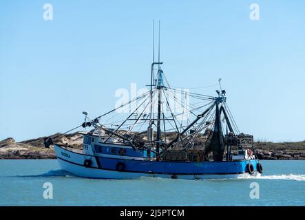 A commercial shrimp boat heads out to see through the Brownsville Ship Channel by South Padre Island, Texas. Stock Photo