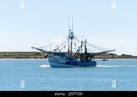 A commercial shrimp boat heads out to see through the Brownsville Ship Channel by South Padre Island, Texas. Stock Photo