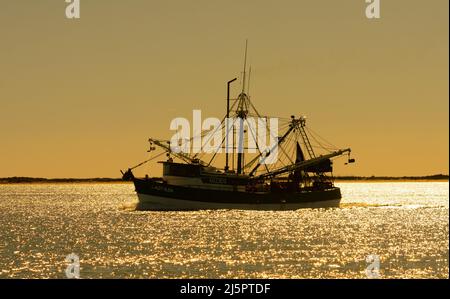 A commercial shrimp boat heads out to see through the Brownsville Ship Channel by South Padre Island, Texas. Stock Photo