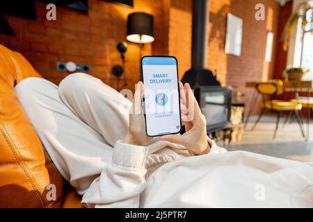 Woman using smart phone with running delivery application at home Stock Photo