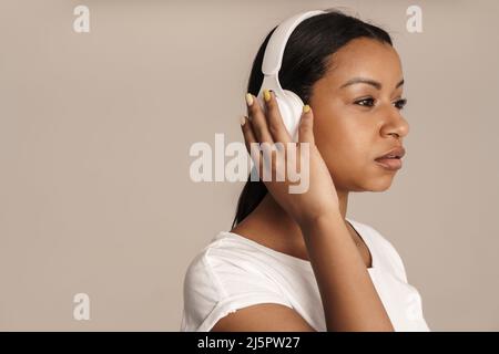 Young black woman wearing t-shirt listening music with headphones isolated over white wall Stock Photo