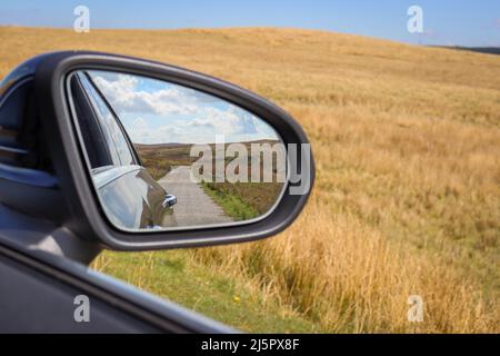 Looking back through a car mirror / open country road / empty road Stock Photo
