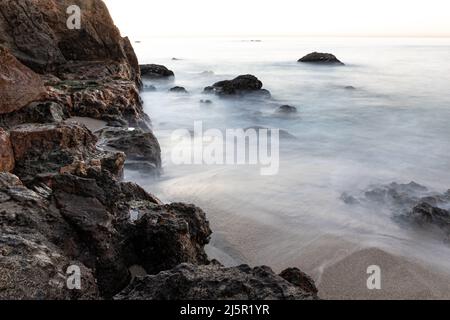 Rocky coastline in the early morning at Malibu, California. Silky waves glide over the sand. Stock Photo