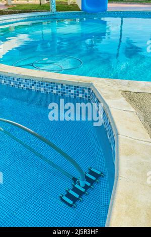 Worker cleaning outdoor pool with underwater vacuum early in the morning. Selective focus Stock Photo