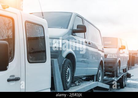 White small cargo truck car carrier loaded with two yellow van minibus on flatbed platform and semi trailer tow on roadside highway road. Volunteer Stock Photo