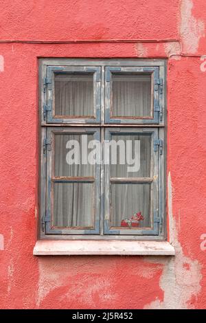 Wooden blue weathered window in red wall Stock Photo