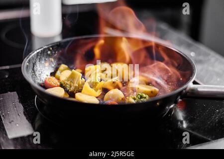 Close-up of pan on cooker with vegetables cooking on open fire in restaurant Stock Photo