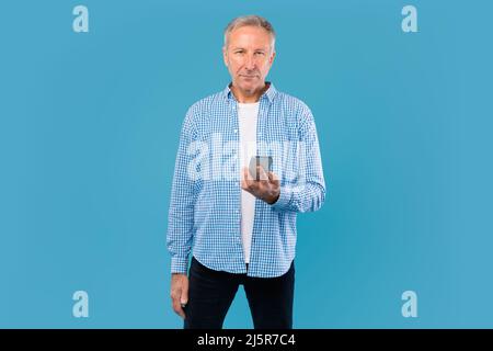 Mature man using his mobile phone at blue studio Stock Photo