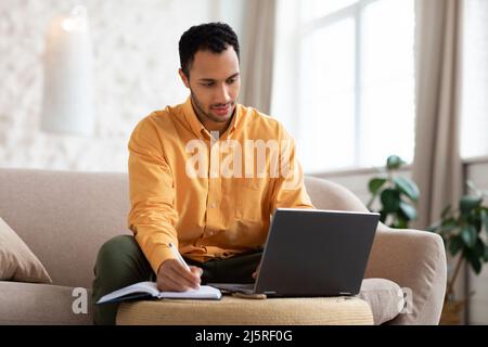 Portrait of focused Arab man using laptop and writing Stock Photo