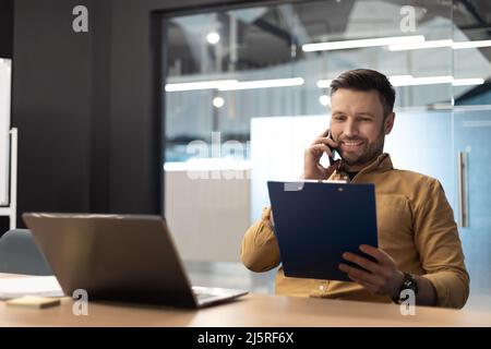 Business Man Talking On Cellphone Holding Papers In Office Stock Photo