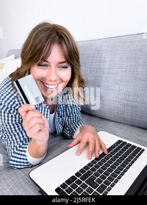 Young woman with credit card shopping over laptop while sitting at home - stock photo Stock Photo