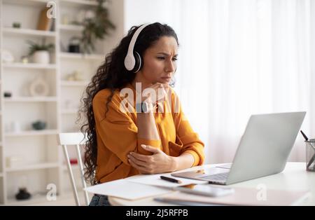 Concerned Middle Eastern Businesswoman Using Laptop Wearing Headphones In Office Stock Photo