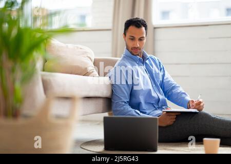 Portrait of young Arab man using laptop and writing Stock Photo