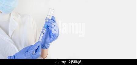Female doctor in a protective blue suit with a syringe on a white background with copy space. Stock Photo