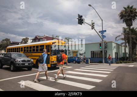 Two young men crossing Mission Bl in front of a yellow school bus in Mission Beach Business District, Mission Bay, San Diego Stock Photo