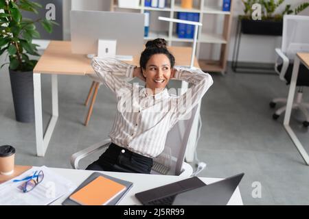 Daydreaming at work. Happy relaxed female entrepreneur resting, leaning back in chair with hands behind head Stock Photo