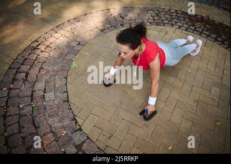 Determined and motivated middle aged African woman of average build in tight sportswear doing push-ups from the floor during a morning workout in a ci Stock Photo