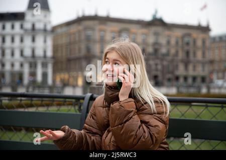 Young girl makes a phone call while sitting on a bench in a park, she is in Scandinavia. Young people and technology Stock Photo