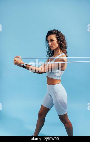 Female athlete stretching resistance band on blue background. Sports woman doing stretching exercises. Stock Photo