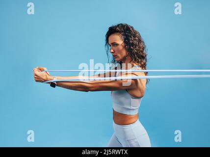 Side view of young fit woman doing intense training with resistance band on blue background Stock Photo