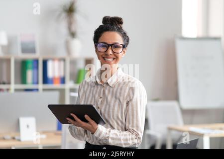 Happy entrepreneur young woman holding digital tablet, using modern technologies in business, office interior Stock Photo