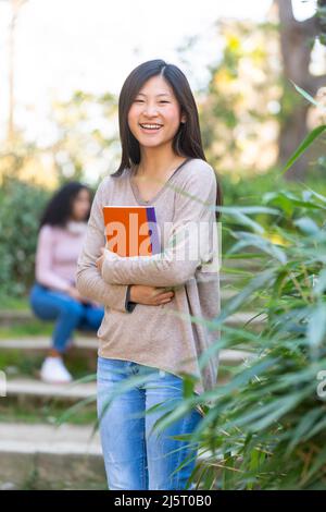 Young asian female student smiling and looking to the camera with a notebook Stock Photo