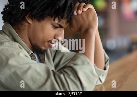 Sad serious concentrated young african american curly male praying or thinking about solving problem Stock Photo