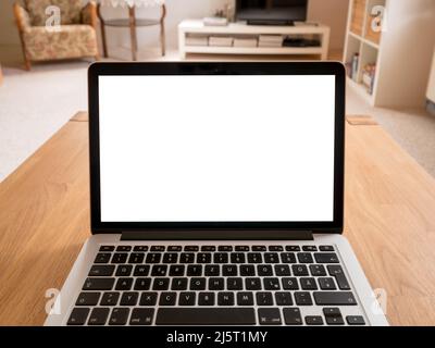 Laptop mockup on a wooden table in a living room. White screen in a home office with point of view of a worker. Computer display and keyboard Stock Photo