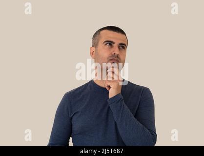 Pensive brown skinned handsome man with short hair standing on isolated background. Stock Photo
