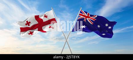 two crossed flags Australia and Georgia waving in wind at cloudy sky ...