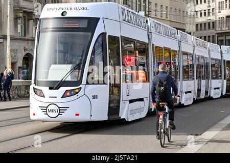 Basel, Switzerland - April 2022: Cyclist riding past one of the city's modern electric trams. The city has an extensive tram network Stock Photo