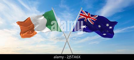 two crossed flags Australia and Ireland waving in wind at cloudy sky ...