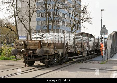 Basel, Switzerland - April 2022: Railway worker watching the end of a train carrying metal ingots crossing a road in the port on the Rhine River Stock Photo