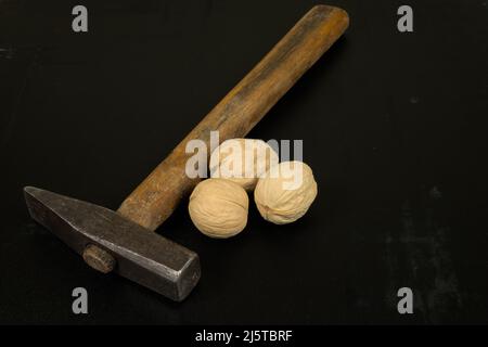 Three walnuts and a hammer on a dark scratched background Stock Photo