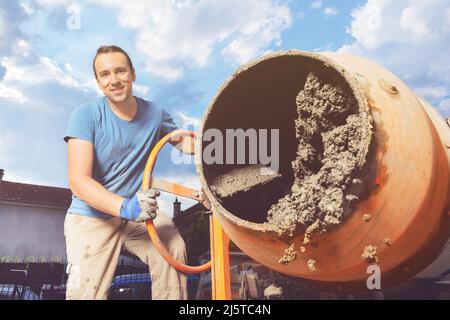 Man tour concrete out of cement mixer at DIY home work Stock Photo