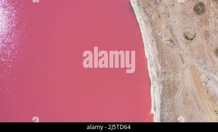 Flying over a pink salt lake. Salt production facilities saline evaporation pond fields in the salty lake. Dunaliella salina impart a red, pink water Stock Photo