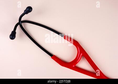 Stethoscope red and black on beige background. Real professional medical equipment. Healthcare, checkup, heart disease concept. Stock Photo