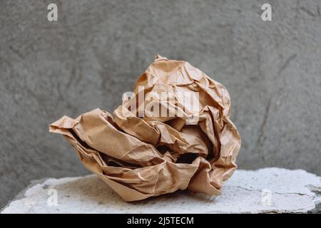 Old kraft paper crumpled into a pile on a stone stand shelf or platform of ancient stone rough texture on a background of gray concrete wall. Copy Space. Stock Photo