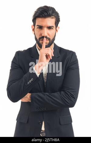 Make silence please Portrait of serious brunette man with beard in suit standing showing quiet gesture, saying hush, keep secret. indoor studio shot isolated on white background. High quality photo Stock Photo
