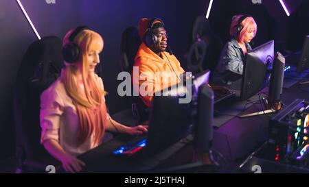 Online gaming team. Three interracial people sitting in an Internet cafe, playing on desktop computers, using professional headset. High quality photo Stock Photo