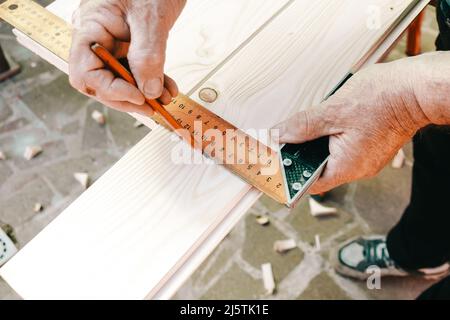 Close-up of craftsman hands in measuring wooden plank with angular ruler and pencil. Woodwork concept. Stock Photo