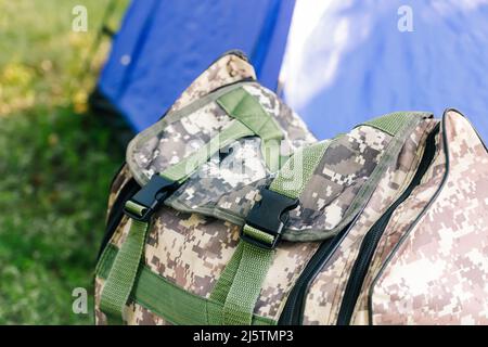 Defocus blue open tourist tent standing on green nature background. Army backpack. Tourism concept. Summer vacation in forest, camping. Wild nature. H Stock Photo