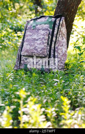 Defocus military backpack. Army bag on green grass background near tree. Military camouflage webbing material on a British army rucksack, backpack. Ve Stock Photo